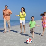 Mother, Father and Children Family Running With Football on Beac